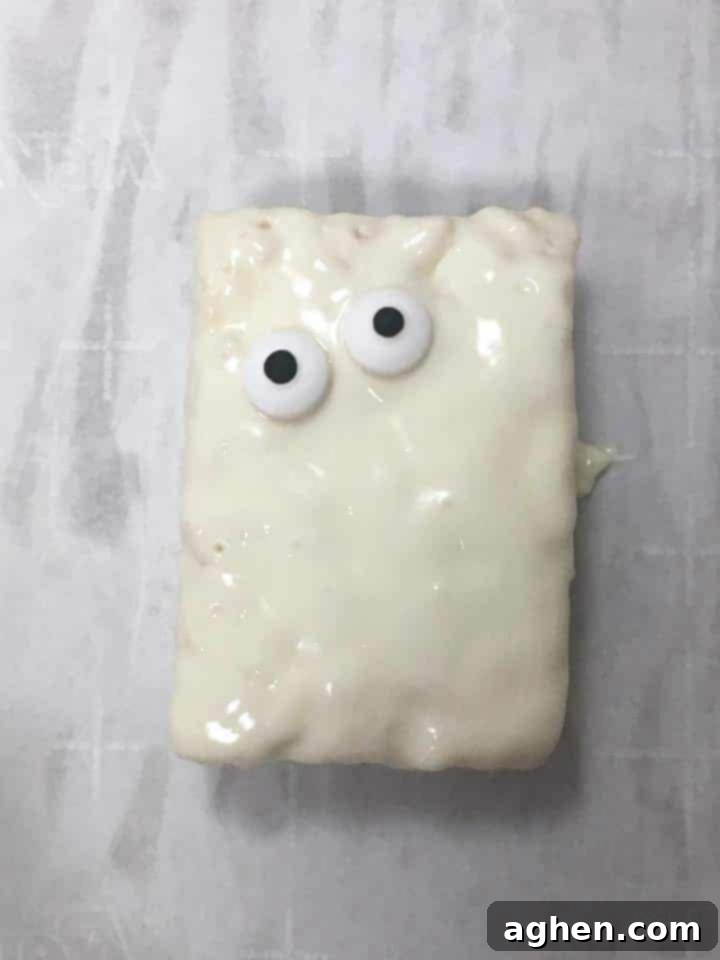 A white chocolate-covered Rice Krispie Treat with two small edible candy eyes already placed, ready for the next step of decoration.