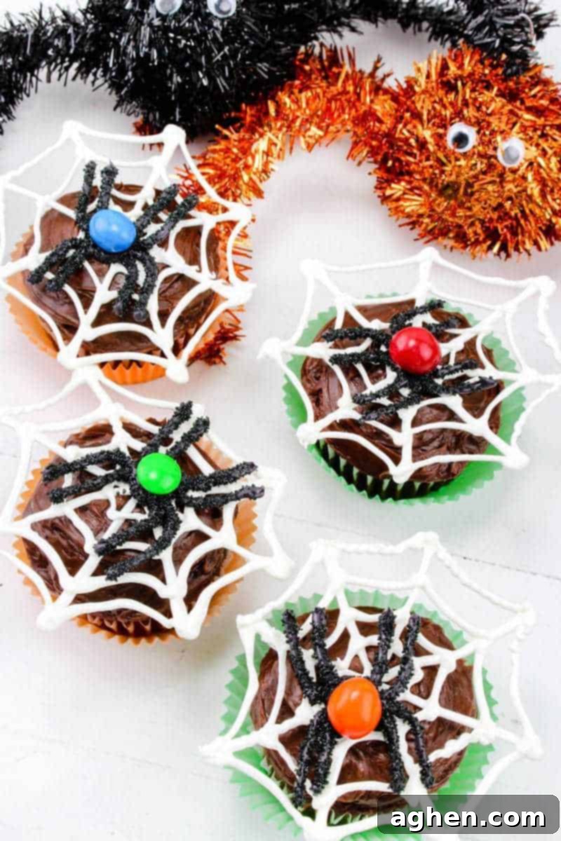 Four Halloween spider web cupcakes with blue, red, green, and orange M&Ms as the spider's bodies, showcasing vibrant spooky desserts.