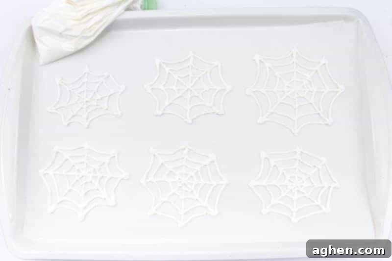 Six delicate white candy spiderwebs piped onto a parchment-lined baking sheet, waiting to set.