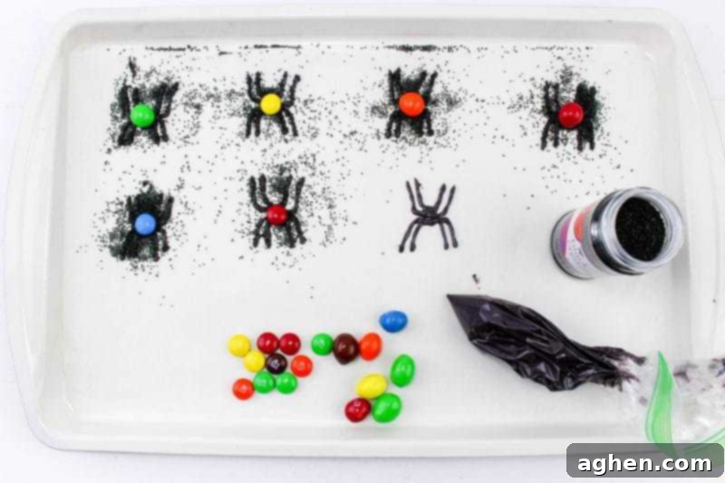 Candy spiders covered with black sanding sugar on a lined baking sheet, with colorful M&Ms forming their bodies.