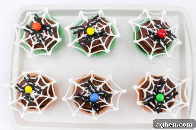 Finished spider web cupcakes arranged on a baking sheet, ready for serving at a Halloween gathering.
