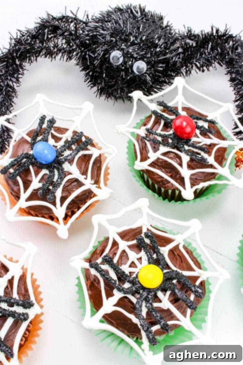 Chocolate frosted cupcakes adorned with intricate white chocolate spider webs and charming black candy spiders, each featuring colorful M&Ms on their bodies.