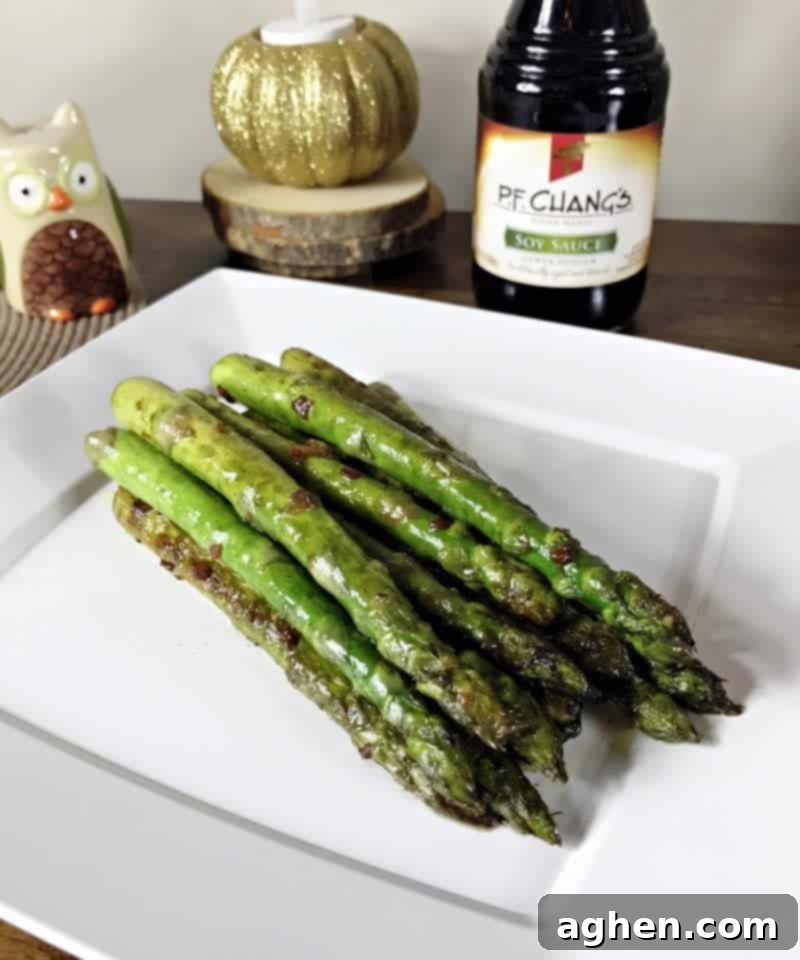 Pan seared asparagus with soy sauce and garlic on a plate with bottle of soy sauce behind it.