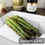 Pan seared asparagus with soy sauce and garlic on a plate with bottle of soy sauce behind it.