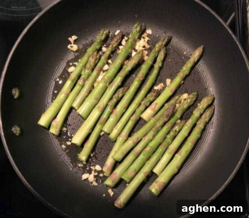 Uncooked asparagus being added to a frying pan with garlic.