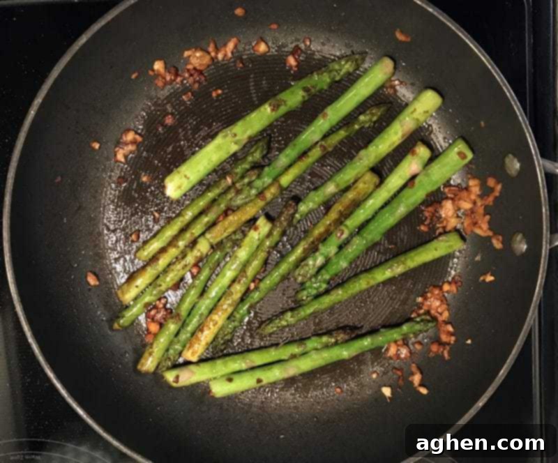 Asparagus cooking in a frying pan with garlic and soy sauce.