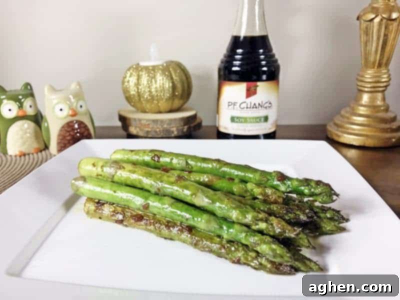 Pan seared asparagus with garlic and soy sauce served on white plate with bottle of P.F.Chang's Soy Sauce in the background.