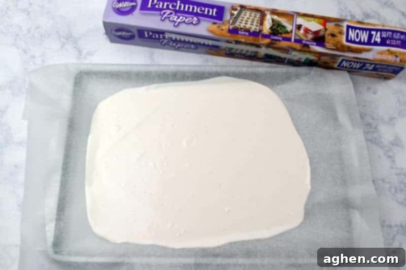 Melted white candy is poured onto a parchment-lined baking sheet, forming the base of the Halloween bark.