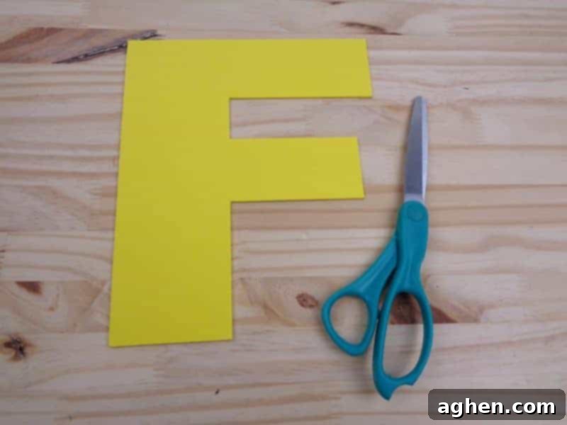 Carefully cutting the traced uppercase Letter F shape from the yellow craft foam with scissors.