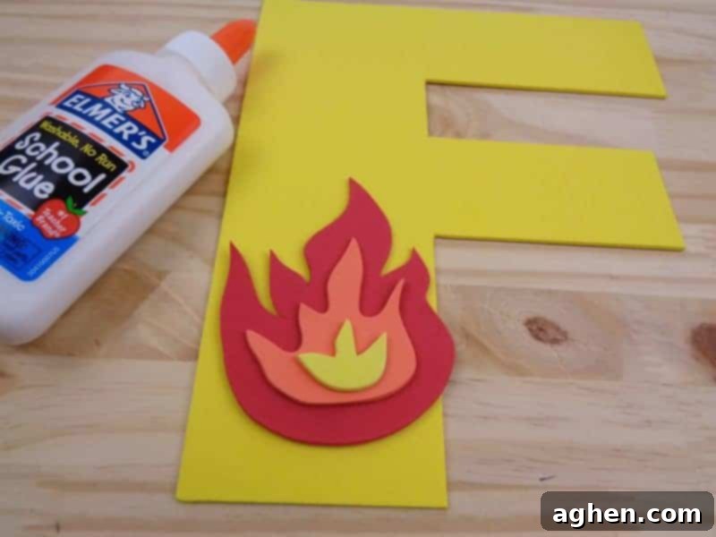 Applying glue to the assembled craft foam fire and carefully adhering it to the cutout Letter F.
