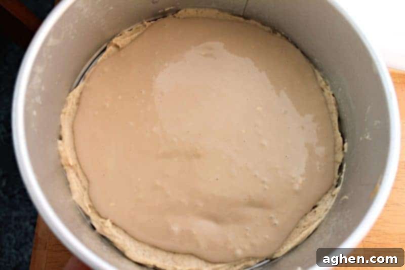 Cream cheese filling being poured over the first cake batter layer in the pan.