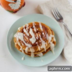 A square image of stacked pumpkin spice pancakes with cinnamon swirls and cream cheese glaze, ready to be served.