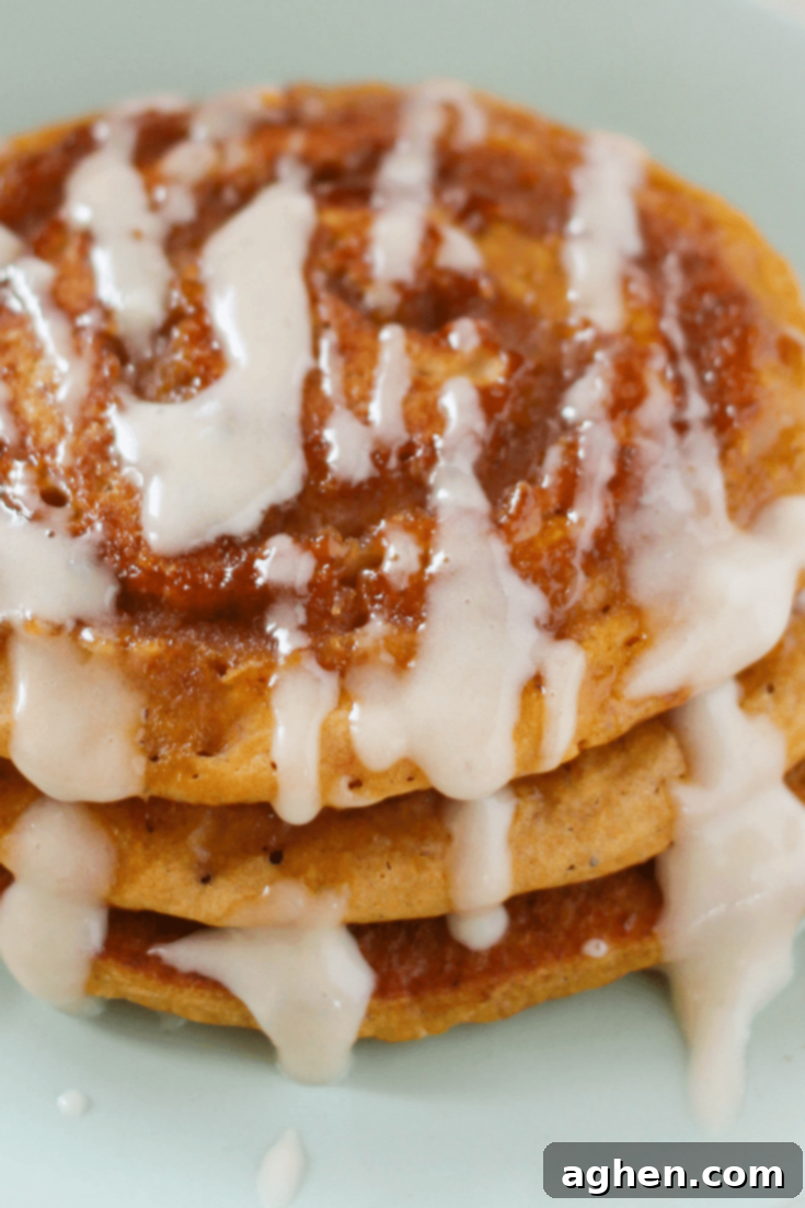 A top-down view of a single fluffy pumpkin spice pancake with a distinct cinnamon swirl pattern and a generous amount of cream cheese glaze, ready to be eaten.