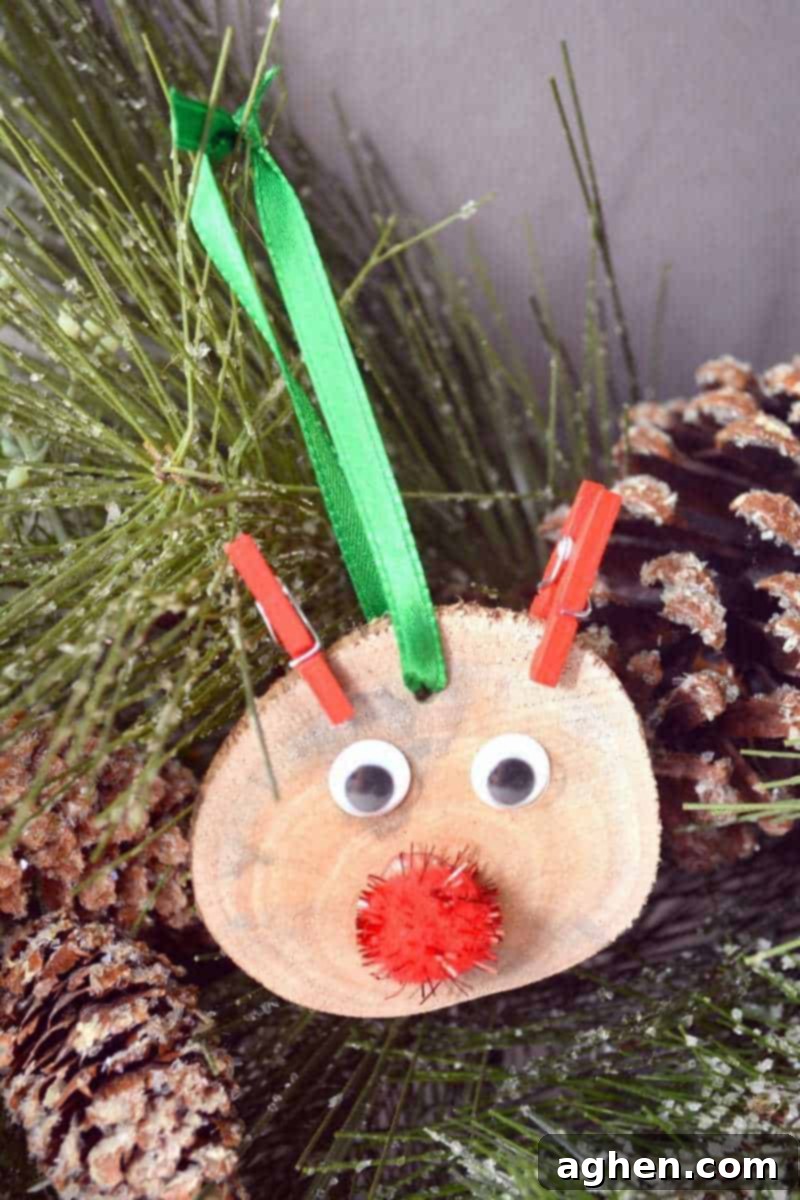 A finished DIY rustic wood slice Rudolph reindeer ornament with googly eyes, a red pom-pom nose, and mini clothespin antlers, ready to hang on a Christmas tree.