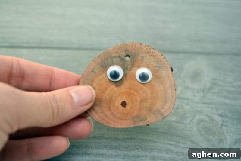 Two googly eyes glued onto the front of a wood slice, creating the start of a reindeer face.