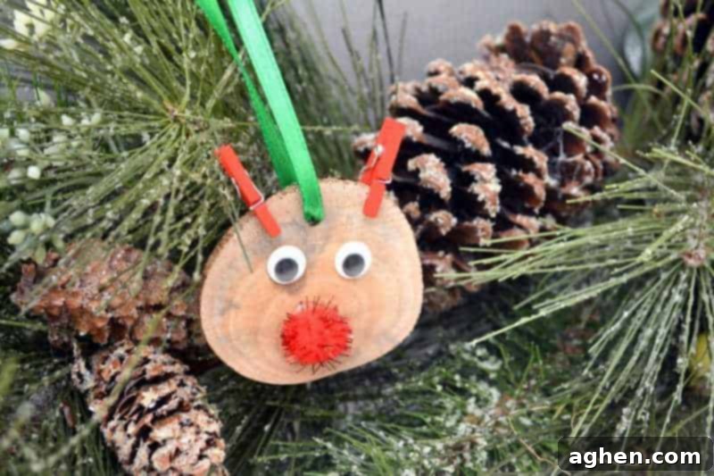 A close-up of a finished DIY rustic wood slice Rudolph ornament, featuring googly eyes, a sparkly red nose, and red clothespin antlers.