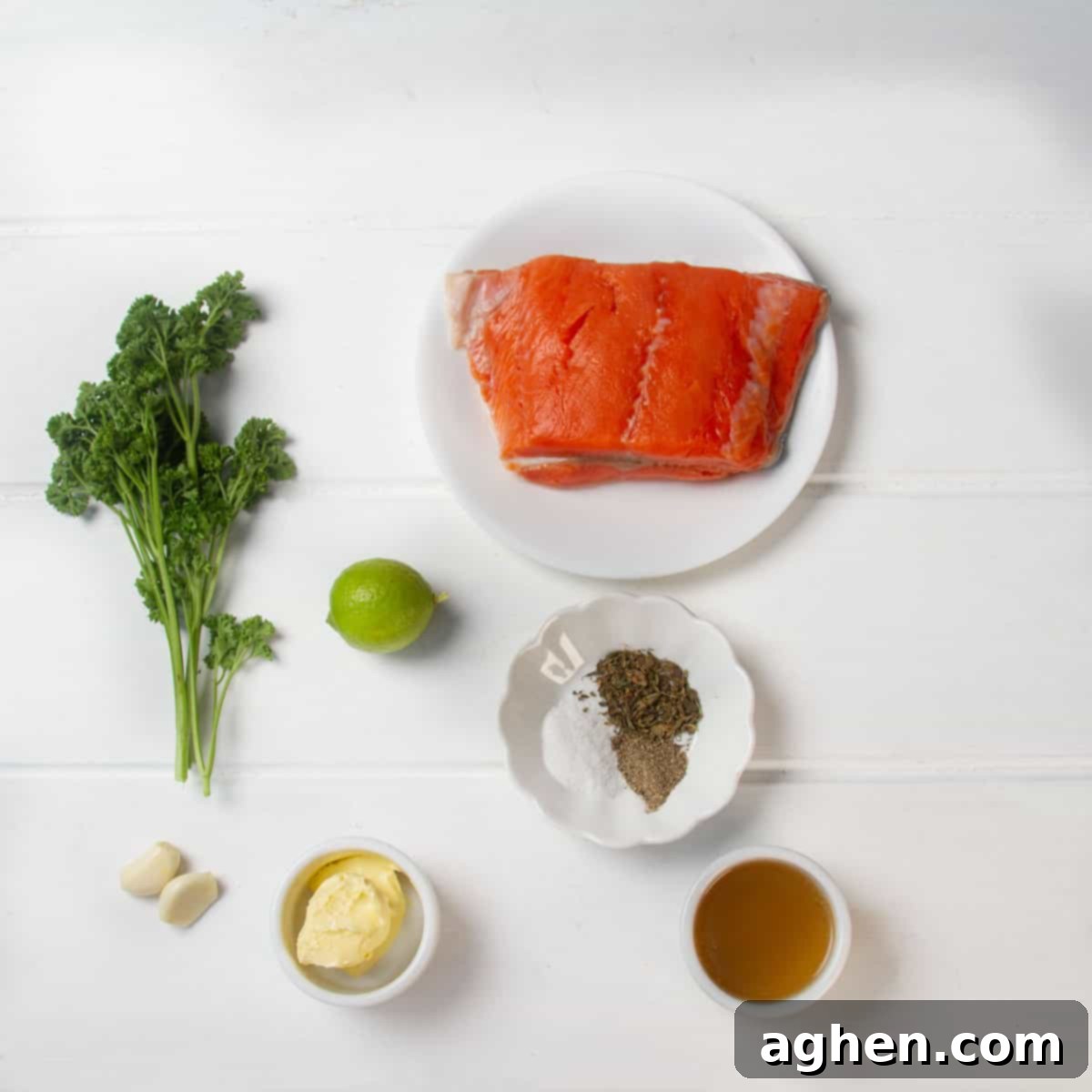 Raw salmon fillet, a bunch of parsley, a lime, seasonings in a dish, softened butter, two garlic cloves, and cornstarch dissolved in broth. 
