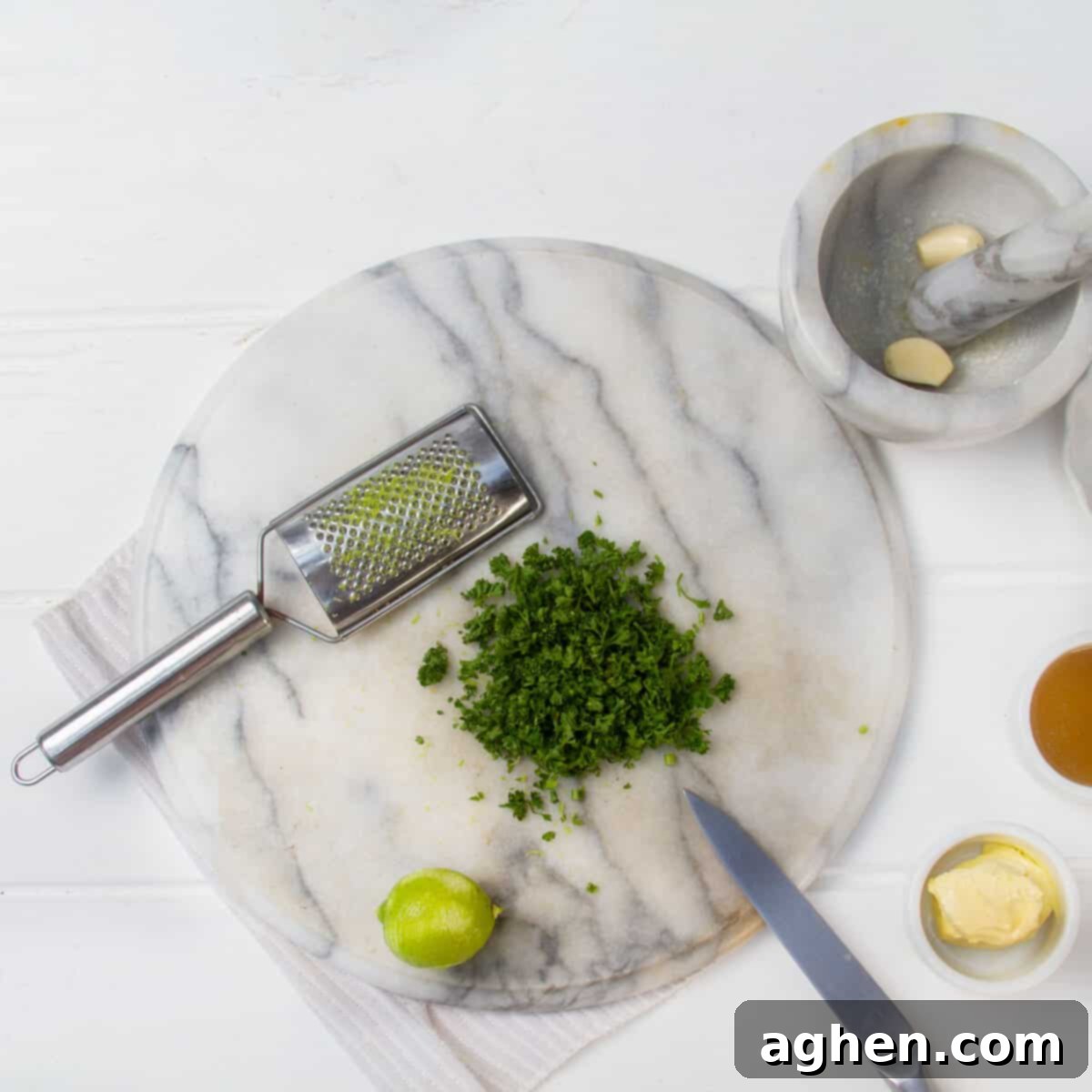 Crushed garlic and finely chopped parsley beside a zested lemon and grater. 
