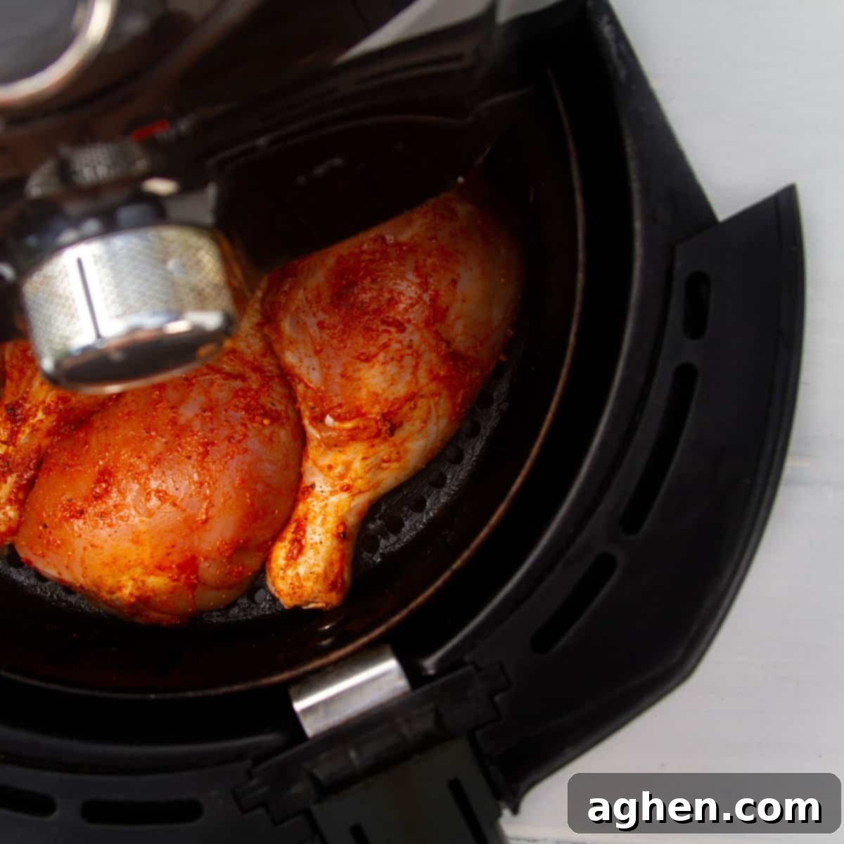 Seasoned chicken thighs in an air fryer basket.