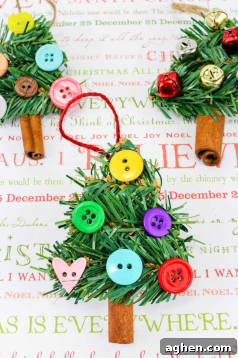 Close-up of a homemade Christmas tree ornament featuring a cinnamon stick base, green garland branches, and colorful buttons and pom-poms.