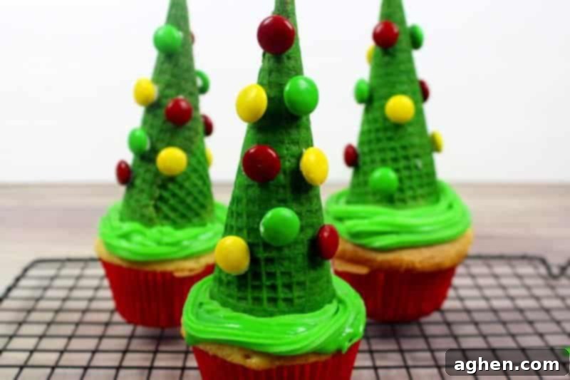 Close-up of a sugar cone Christmas tree cupcake being decorated with colorful M&Ms, adding festive ornaments to the green cone.