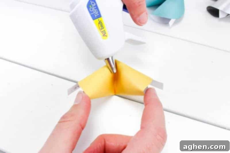 Applying hot glue to the inner crease of the paper fortune cookie.