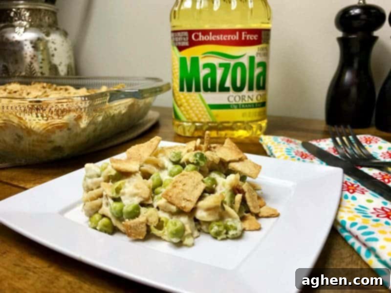 A large baking dish filled with a creamy, golden-brown tuna pasta casserole, ready to be served. It features visible multi-grain pasta, peas, and a golden cracker topping.