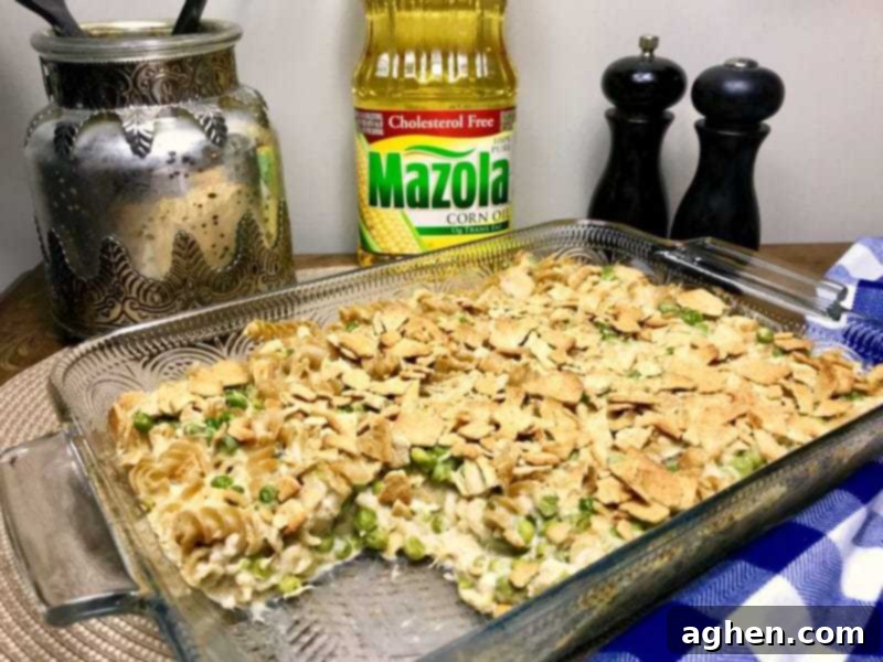 A freshly baked tuna pasta casserole with peas, served in a white baking dish. The top is golden brown with a crispy cracker crust.