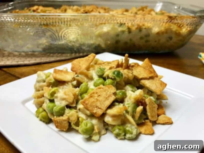 A close-up of a serving of healthy tuna pasta casserole with peas, showing the creamy texture and the golden brown topping.