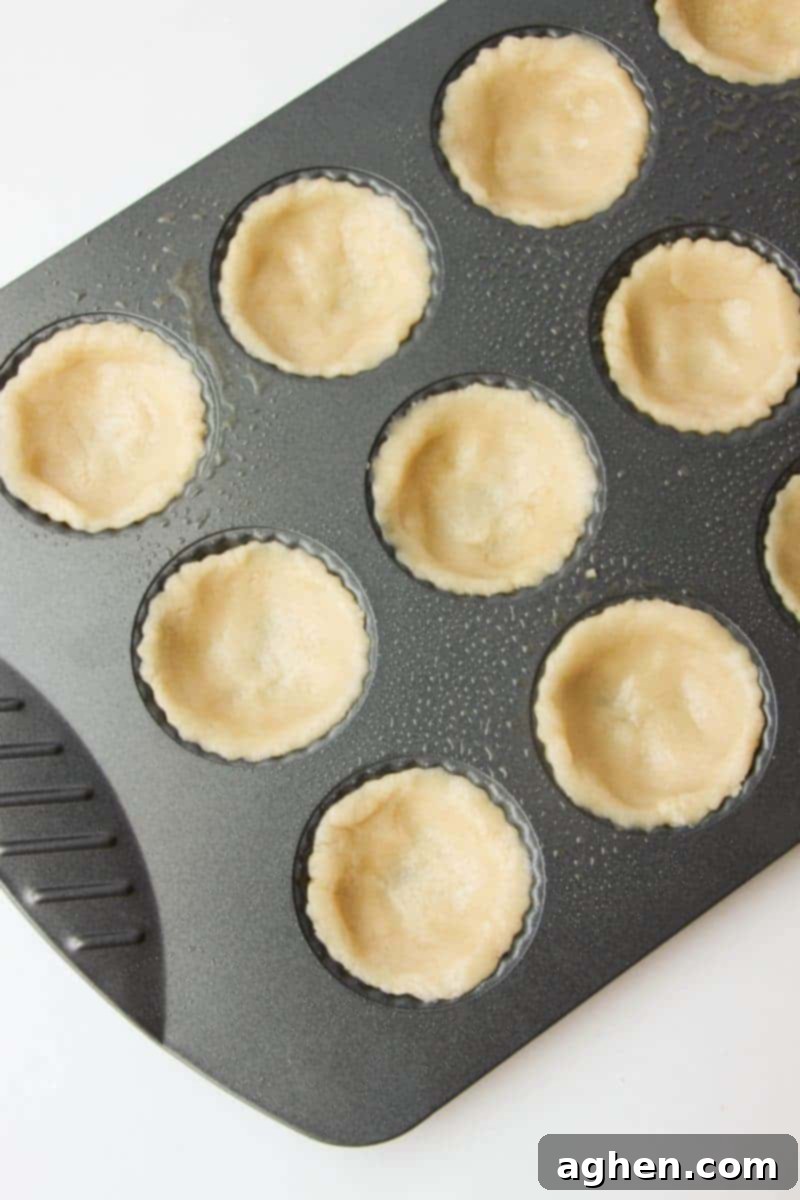 Preparing the sugar cookie cups by pressing dough into a muffin tin, creating a perfect base for the creamy banana filling.