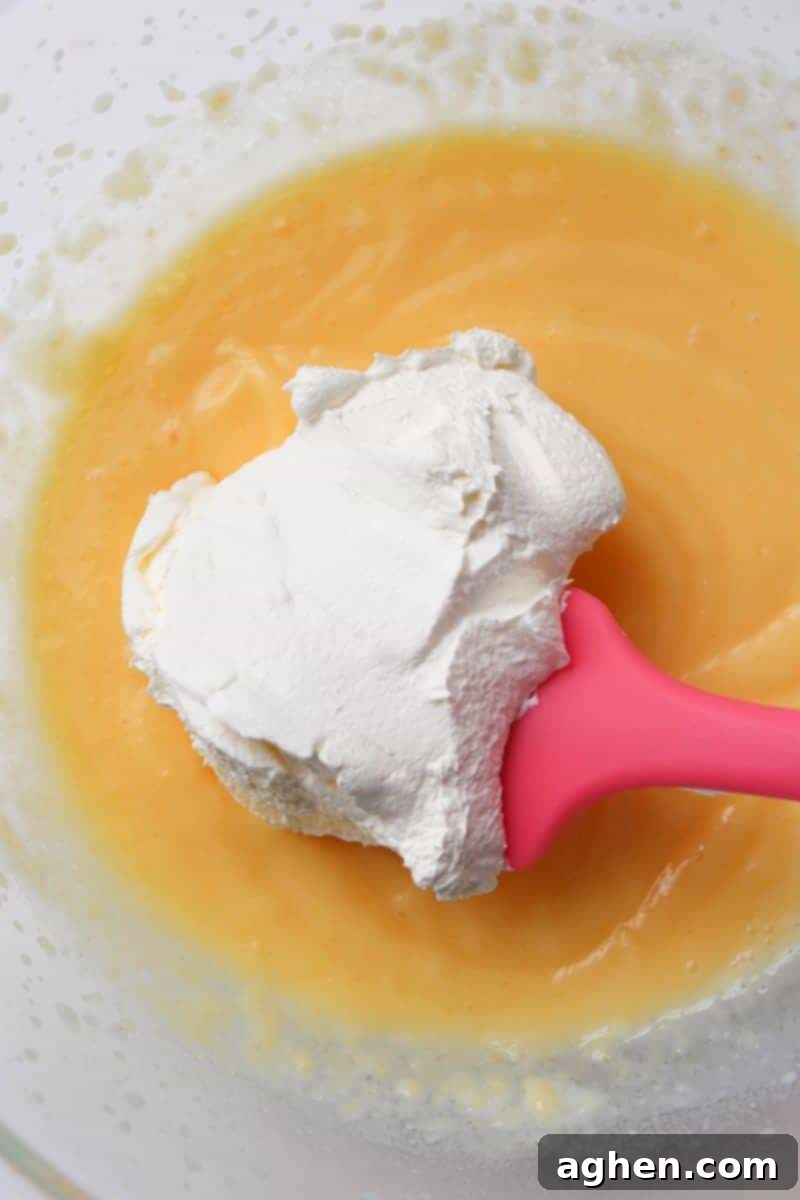 Gently folding whipped topping into the banana pudding mixture, creating a light and airy banana cream filling.