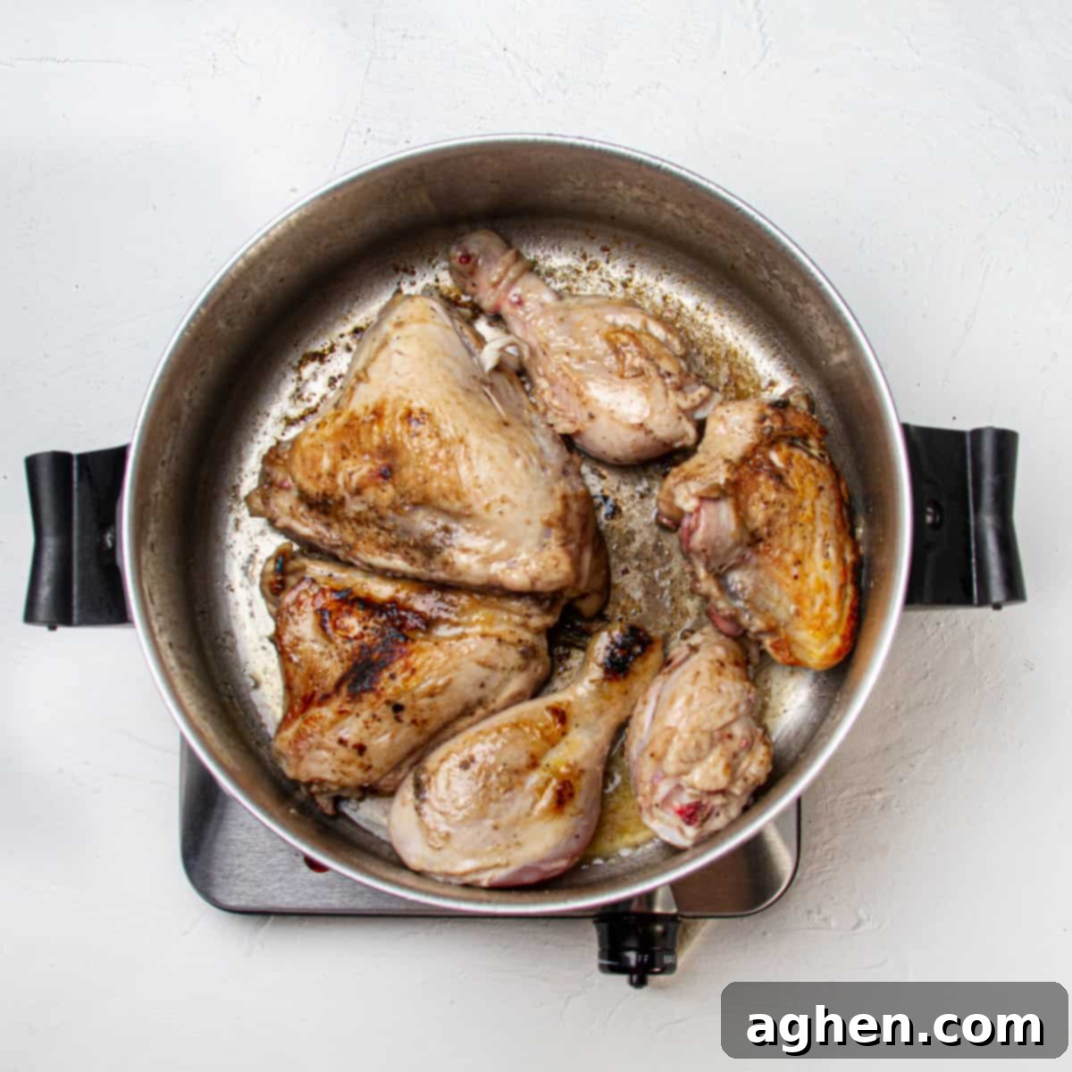 Chicken thighs searing in a hot pan to develop a golden-brown crust.