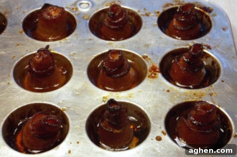 Candied bacon roses baking in a mini muffin tin, with sugar caramelizing and bacon crisping.