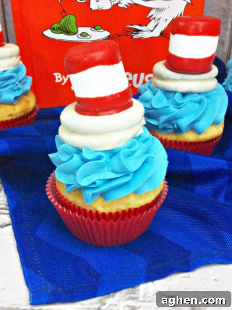 Close-up of a Cat in the Hat cupcake, showing the sky-blue swirled frosting and a detailed red and white striped hat topper made from marshmallows and chocolate dipped Oreos.
