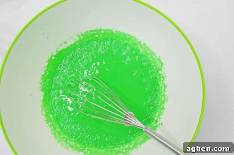 Step-by-step: Whisking green gel food coloring into the pudding mixture to achieve a vibrant green color.