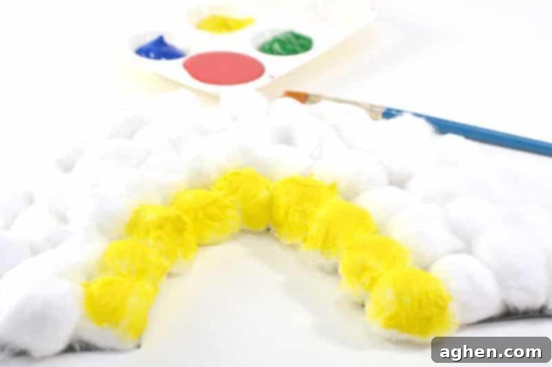 Pressing cotton balls onto the glue-covered rainbow shape.