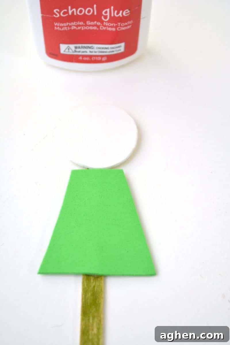 Step-by-step instruction: Attaching the green foam shirt shape onto the front of the popsicle stick, below the head, for the St. Patrick's Day leprechaun puppet.