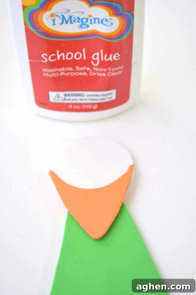 Step-by-step instruction: Gluing the orange beard shape on top of the white head, creating the leprechaun's distinct facial feature on the popsicle stick craft.
