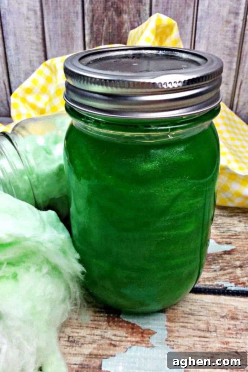 Close-up of a mason jar filled with shimmering green cotton candy moonshine, highlighting its vibrant color and sparkle.