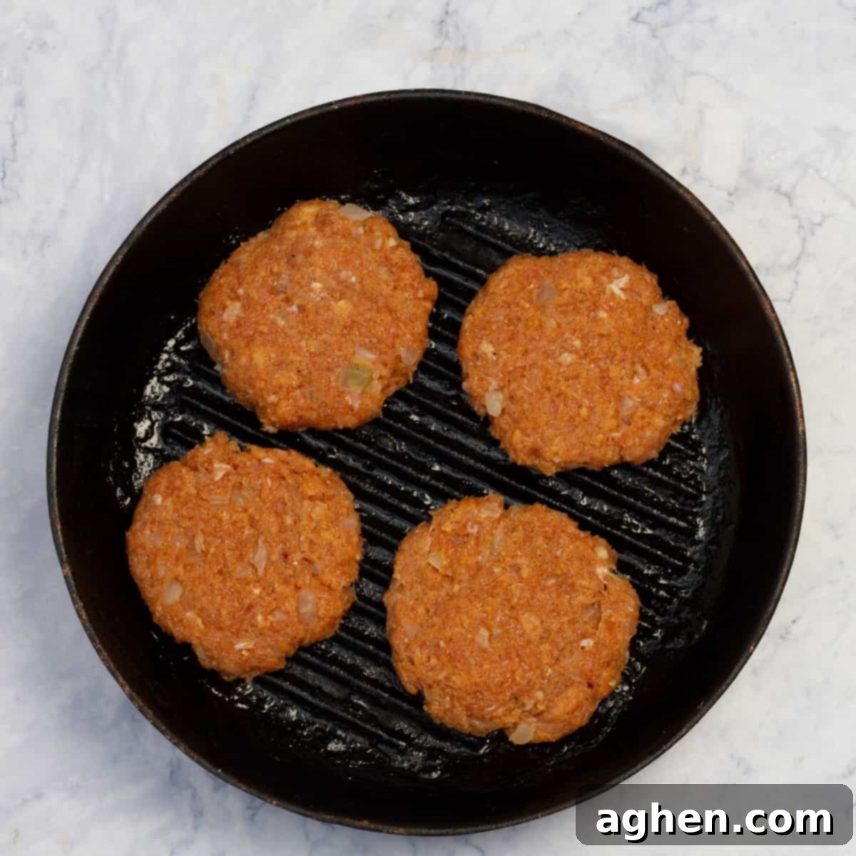 Raw chicken burger patties cooking in a hot skillet.