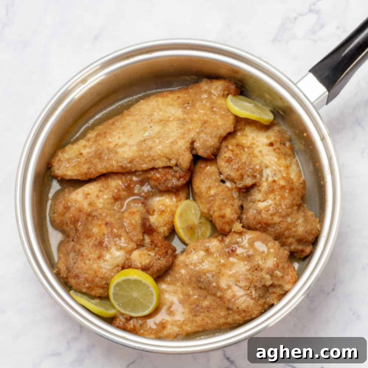 Chicken Francese cooking in a hot pan with lemon slices.