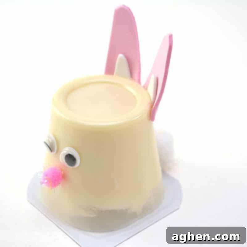 Step 8: Glue a medium white pom pom to the bottom back of the pudding cup, below the ears, to form the fluffy bunny tail.