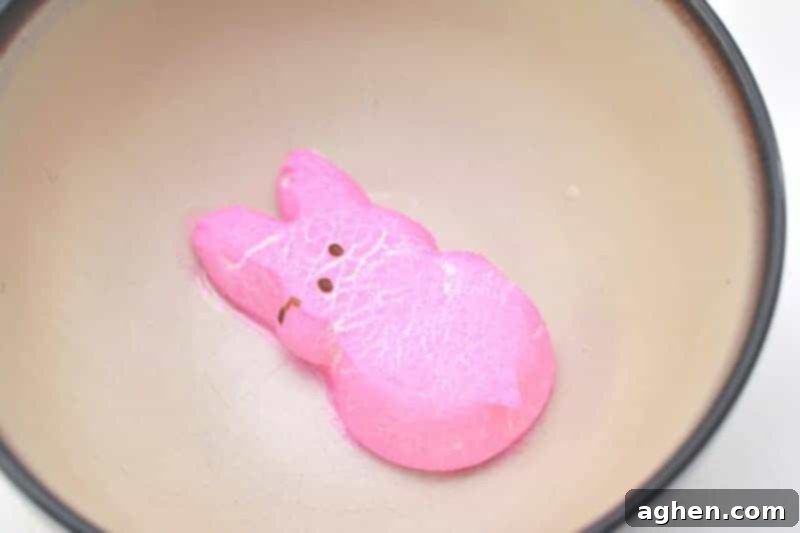 A single pink Peeps marshmallow dramatically puffing up inside a clear microwave-safe bowl after being heated.