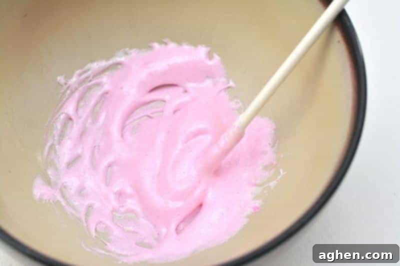 A close-up view of a stirring stick mixing the recently microwaved and softened Peeps marshmallow into a smooth, thick consistency.