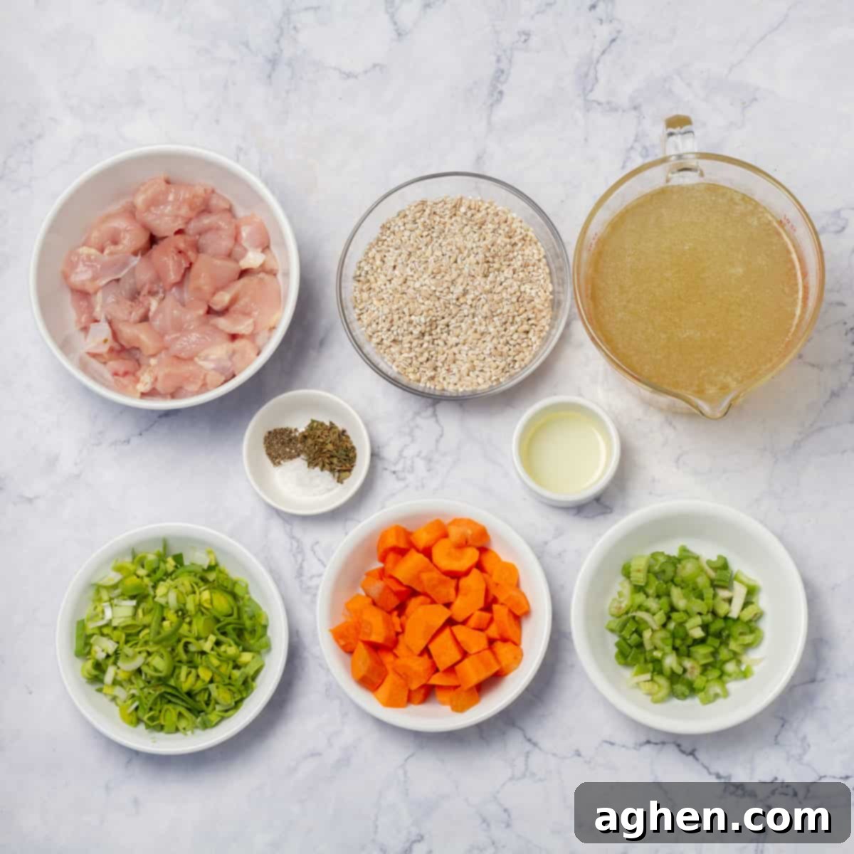 Ingredients of chicken breast and broth, chopped onion, carrots, and celery, and spices in separate dishes, ready for cooking.