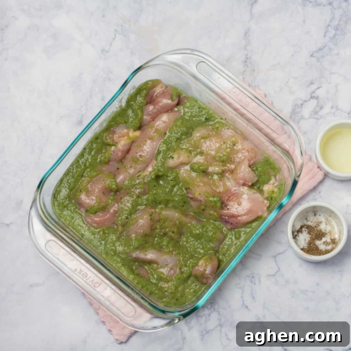 Seasoned chicken marinating in salsa verde sauce in a baking dish, topped with cheese. 
