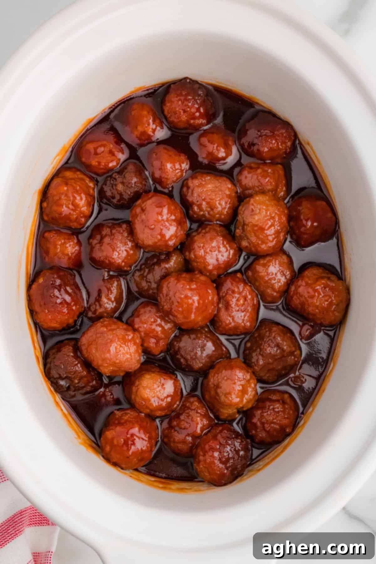 A top-down view of a crockpot filled with meatballs in grape jelly and barbecue sauce. The thickened sauce creates a deep red glaze over the meatballs.