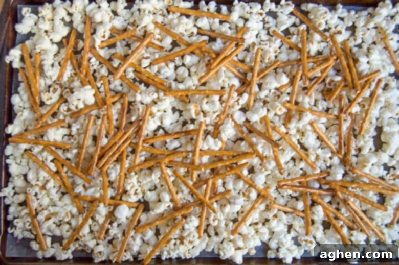 Popcorn and pretzel sticks spread on a baking sheet.