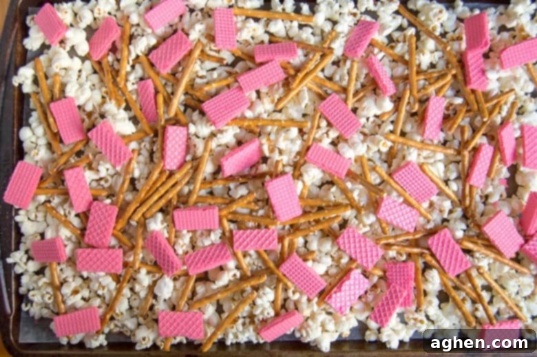 Popcorn, pretzels, and chopped strawberry wafers layered on a baking sheet.