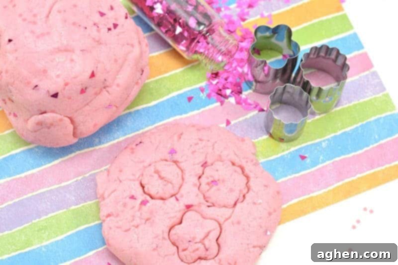 A close-up shot of the vibrant glittery pink princess playdough, showcasing its smooth texture and shimmer. This easy homemade no-cook playdough is made with cake mix, icing, food coloring, olive oil, and glitter, perfect for creative play. An edible version can be made with edible glitter for added safety.